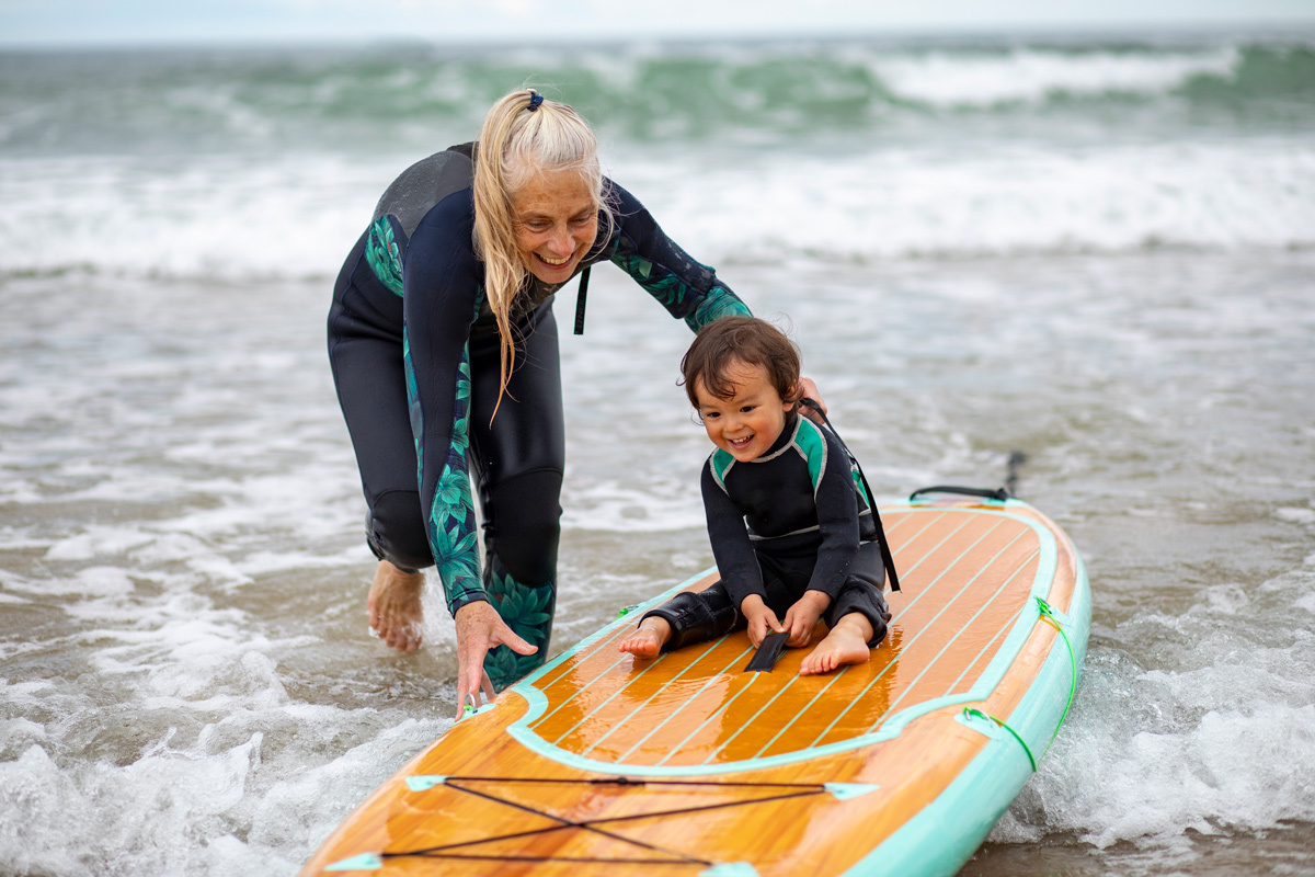 Grandmother helping young grandchild paddle board in the sea