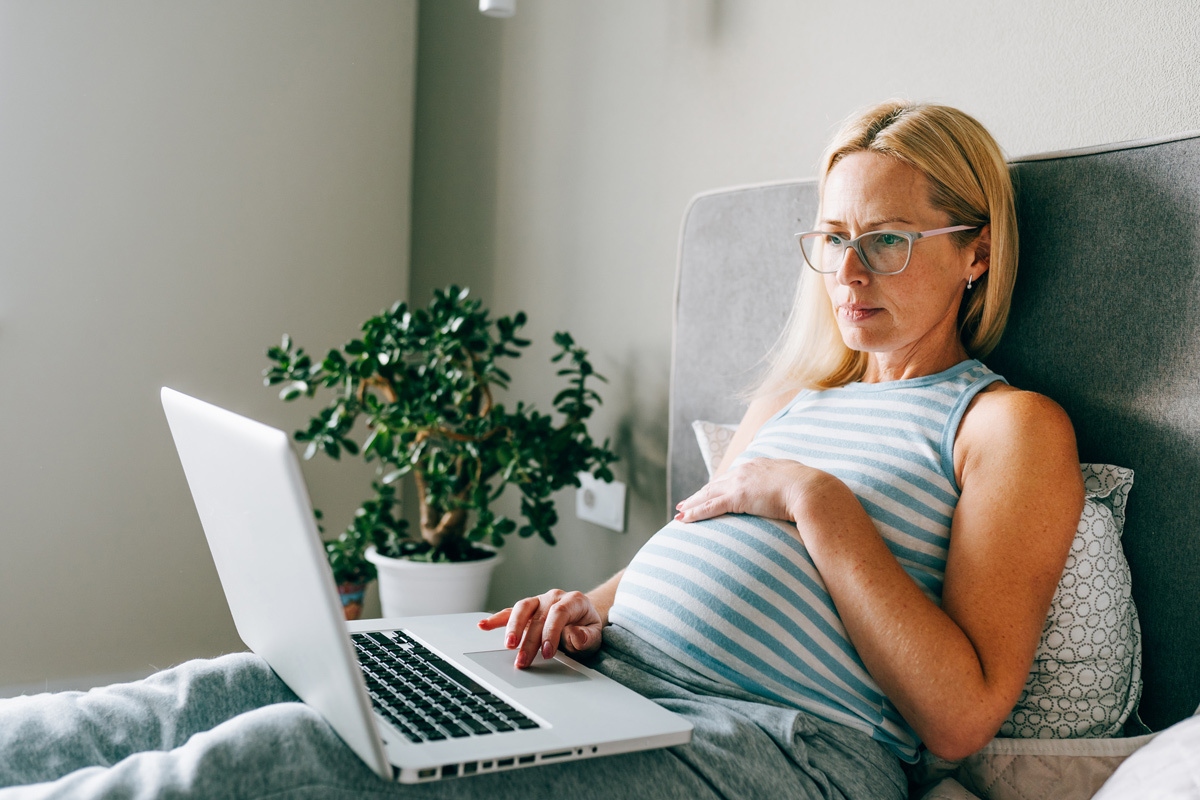 Pregnant women sitting on her bed looking at her laptop