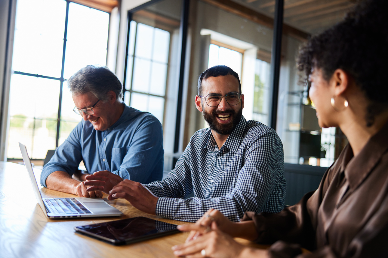Two males and women female sitting at a desk laughing