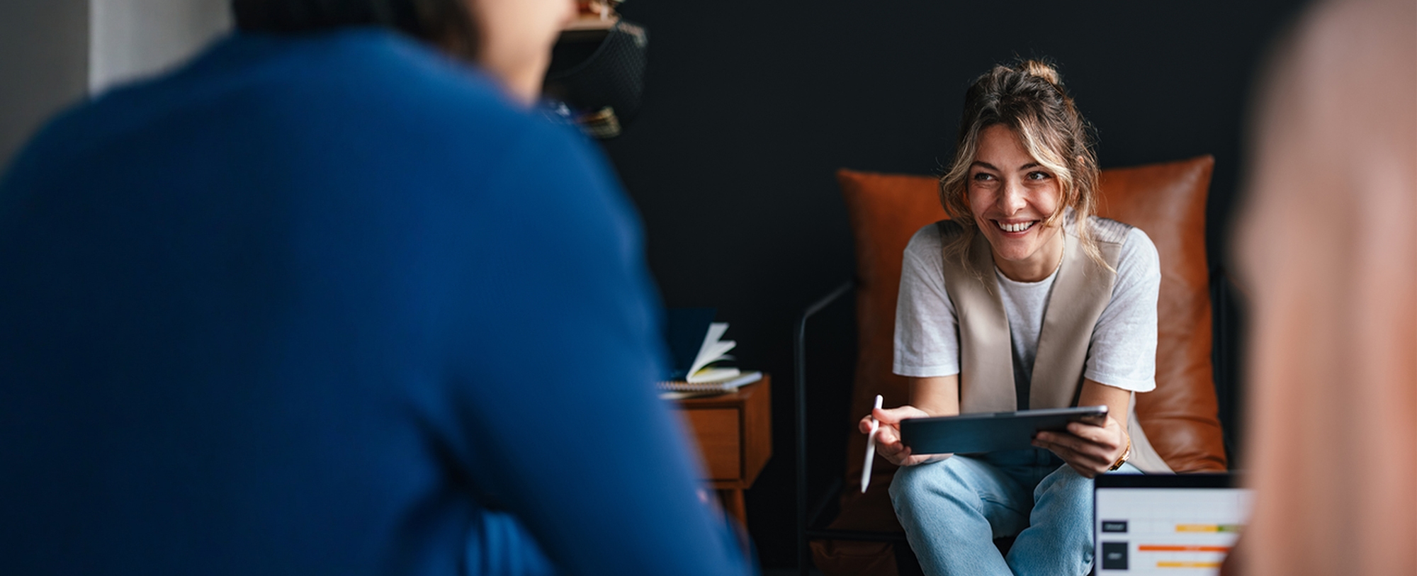 Women sitting with her tablet smiling and chatting to two people