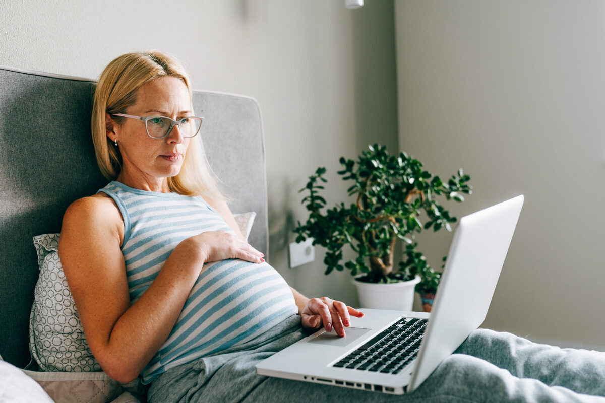 Pregnant women sitting in bed looking at her laptop