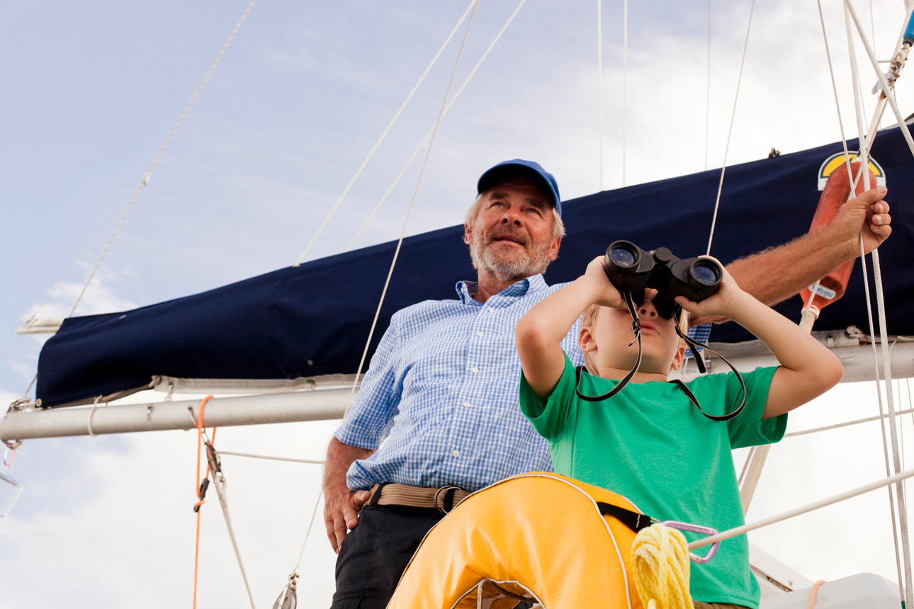 Grandfather and grandson sailing. Grandson looking throgh binoculars