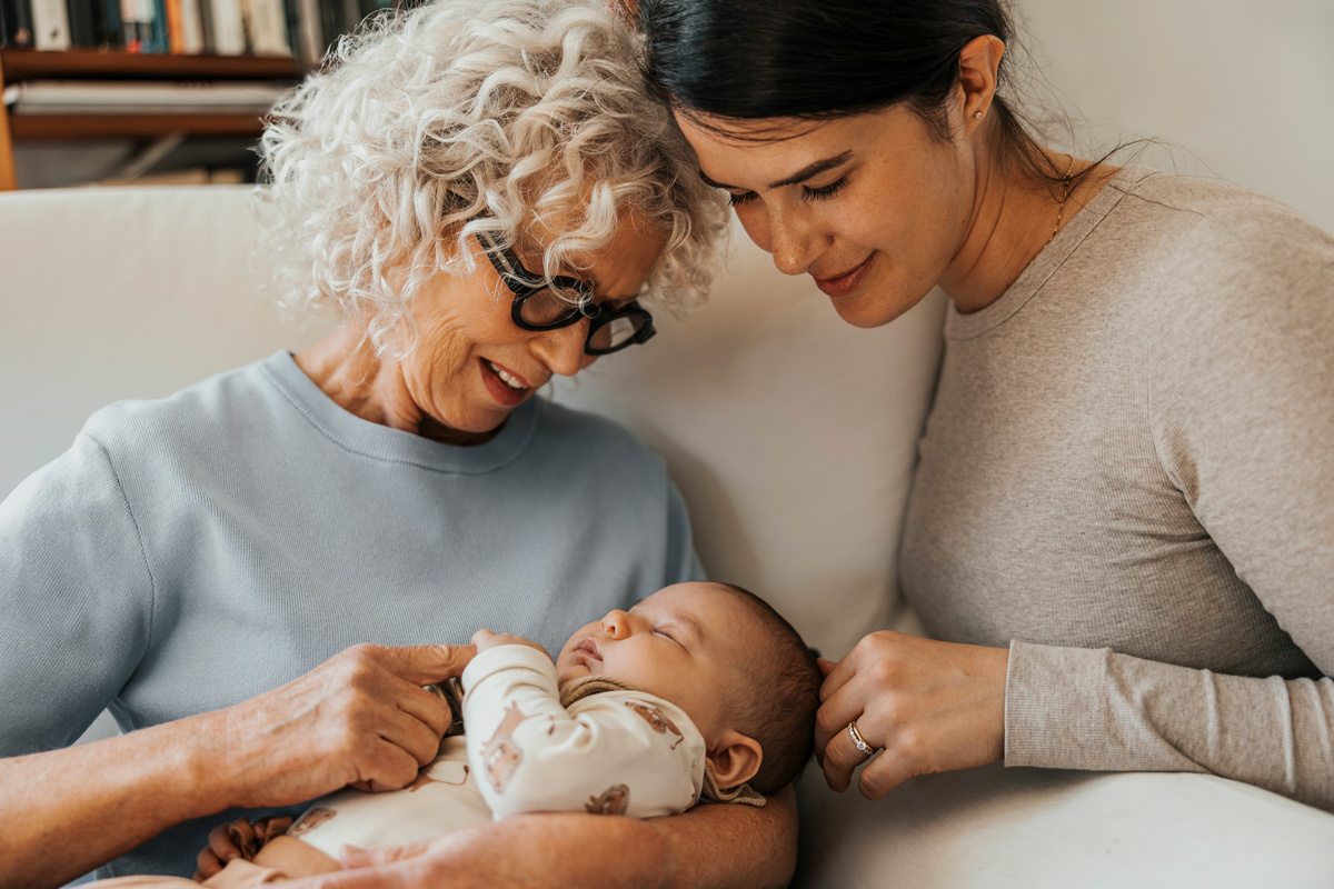 Grandmother holding new born baby whilst mother looks over