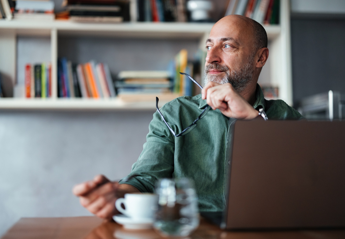 Man holding his glasses looking in the distance with his laptop