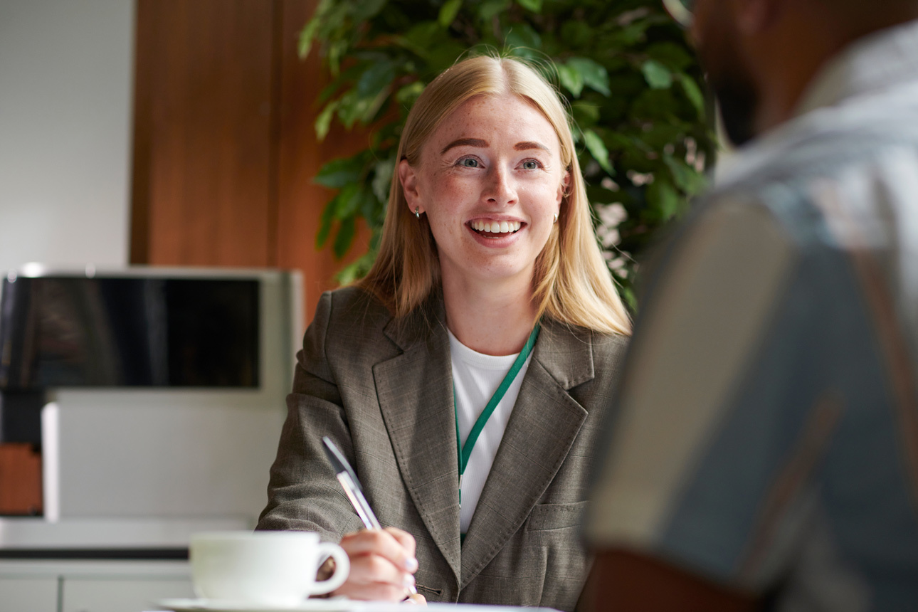 Women smiling as she write notes whilst chatting to a colleague
