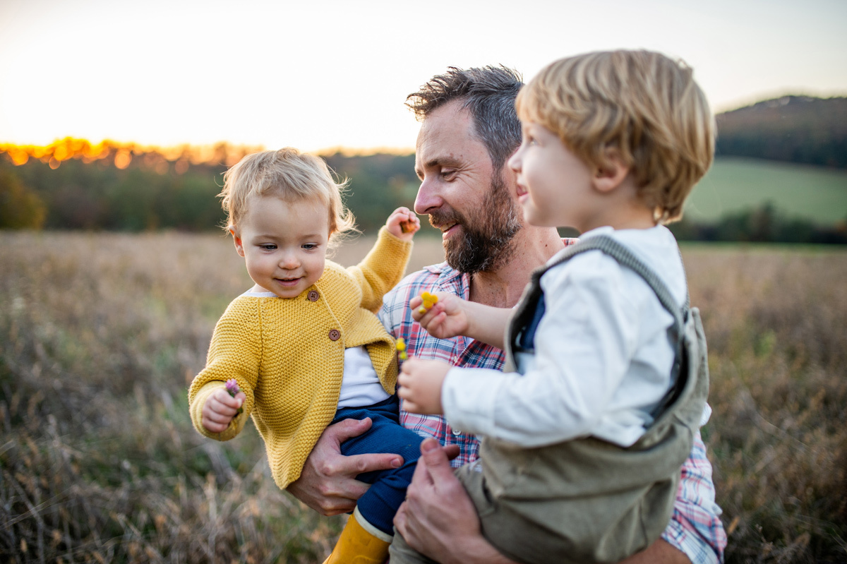 Man carrying his two children walking in a field
