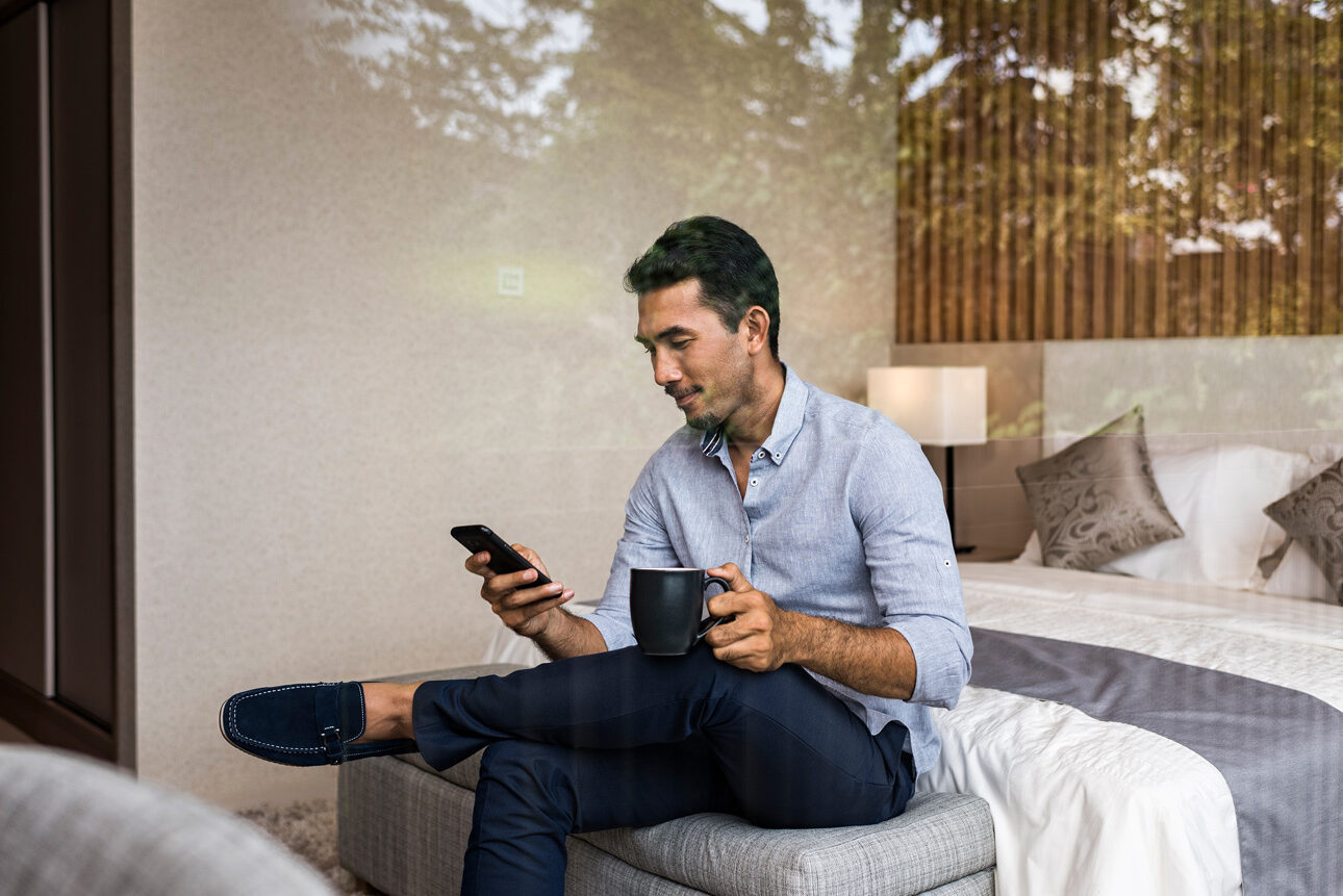 Man sitting on the end of his bed looking at mobile