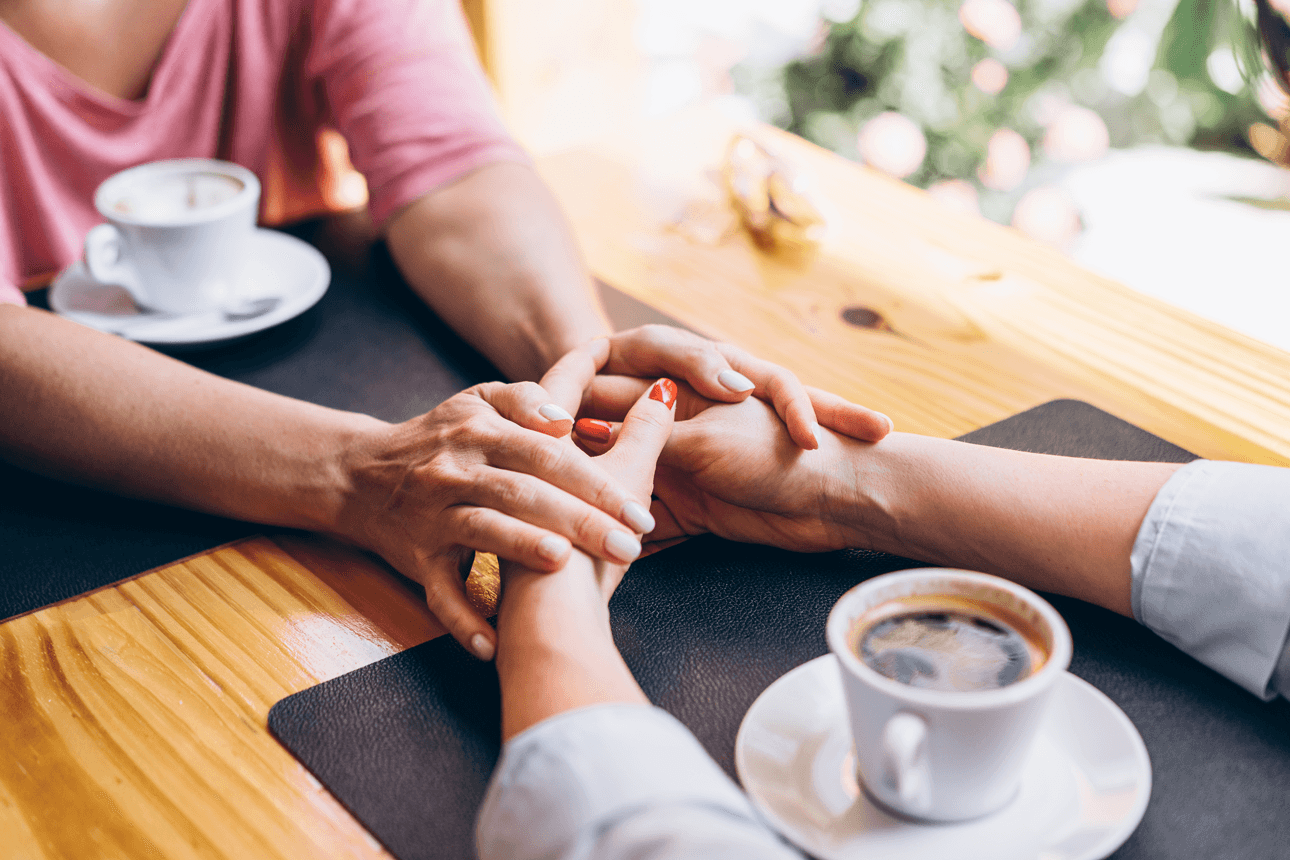 Two people holding hands across the table at a cafe