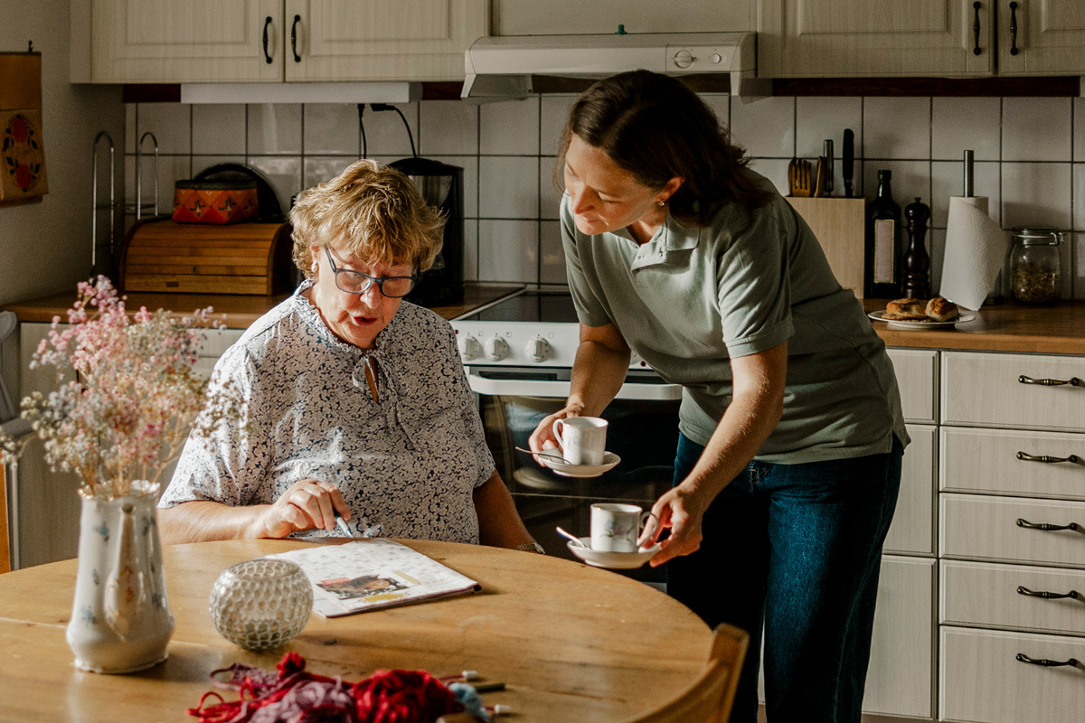 Women sitting at a kitchen table whilst young women hands her cup